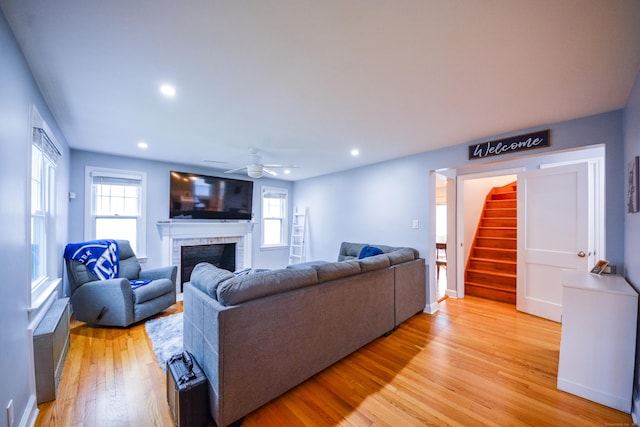living area featuring a brick fireplace, light wood-type flooring, stairs, a ceiling fan, and recessed lighting