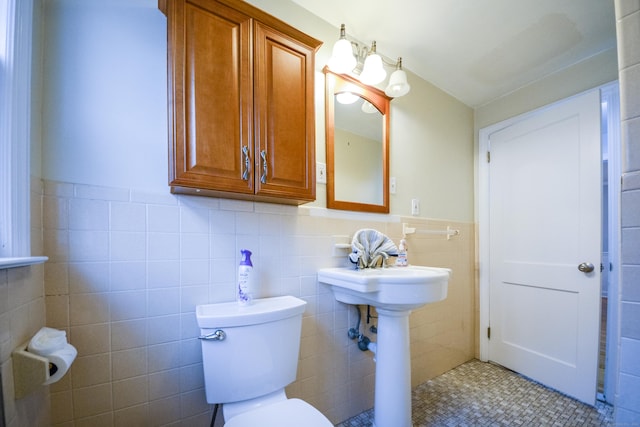 bathroom with tile walls, wainscoting, toilet, and a sink