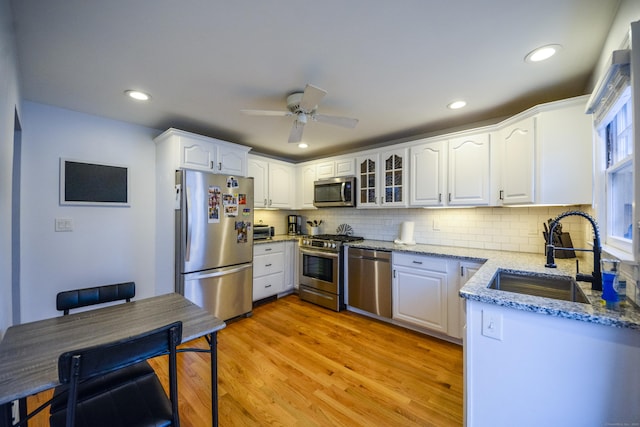 kitchen with appliances with stainless steel finishes, a sink, light stone counters, white cabinets, and light wood-style floors