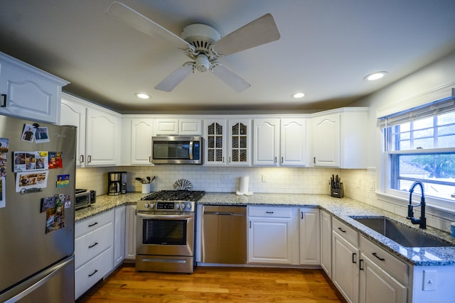 kitchen featuring appliances with stainless steel finishes, a sink, white cabinetry, ceiling fan, and tasteful backsplash