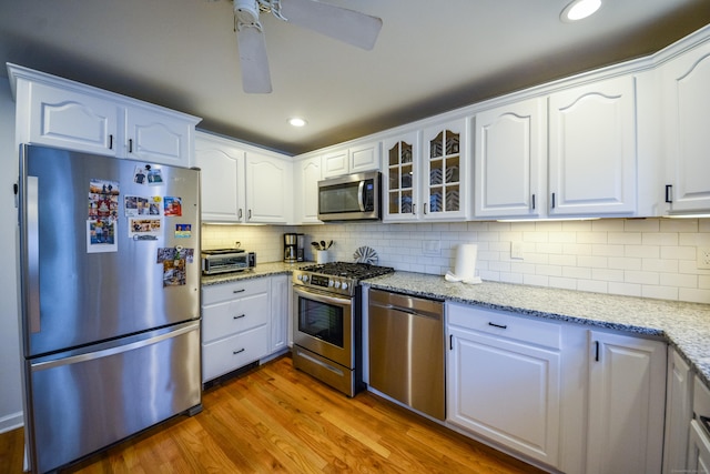 kitchen featuring stainless steel appliances, wood finished floors, white cabinets, glass insert cabinets, and light stone counters
