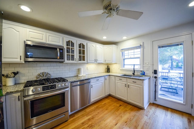 kitchen with appliances with stainless steel finishes, a sink, white cabinets, decorative backsplash, and light wood-type flooring