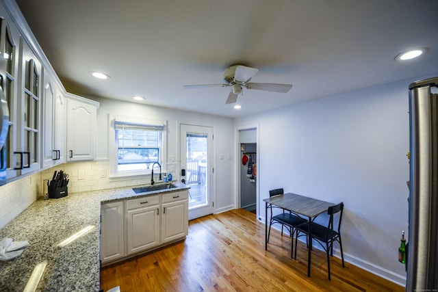 kitchen with a sink, white cabinetry, tasteful backsplash, wood finished floors, and ceiling fan