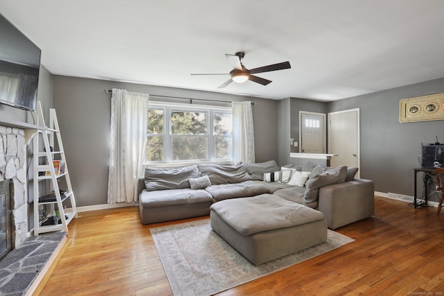 living room featuring a ceiling fan, a fireplace, baseboards, and wood-type flooring