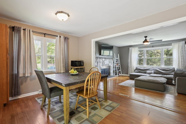 dining space with hardwood / wood-style flooring, healthy amount of natural light, baseboards, and a stone fireplace