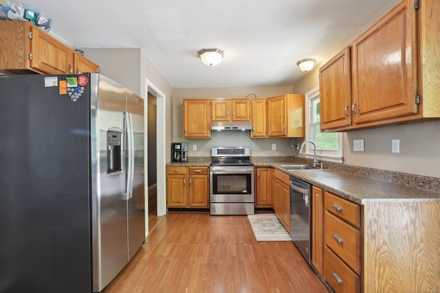 kitchen with stainless steel appliances, a sink, light wood-type flooring, under cabinet range hood, and brown cabinetry