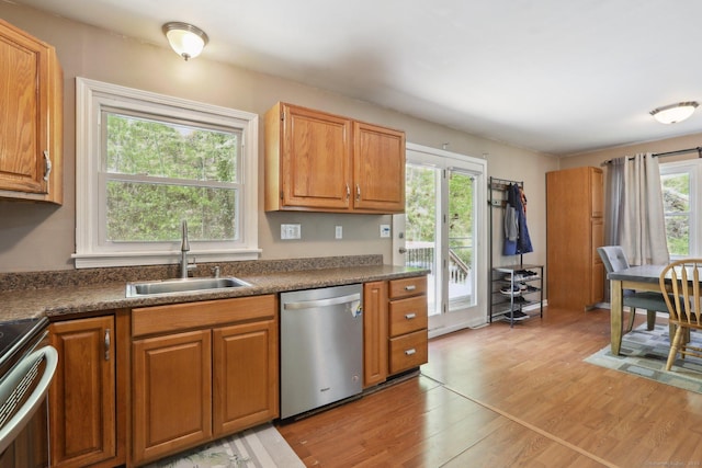 kitchen featuring dishwasher, a sink, range, light wood-style floors, and dark countertops