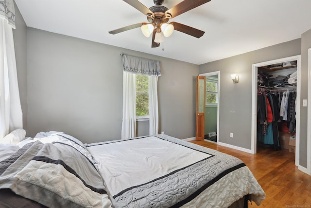 bedroom featuring wood finished floors, a spacious closet, baseboards, a closet, and ceiling fan