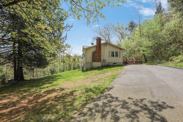 view of home's exterior with a chimney, stairway, a yard, driveway, and a wooden deck