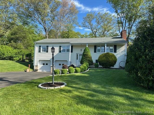 bi-level home featuring asphalt driveway, a chimney, a garage, and a front lawn