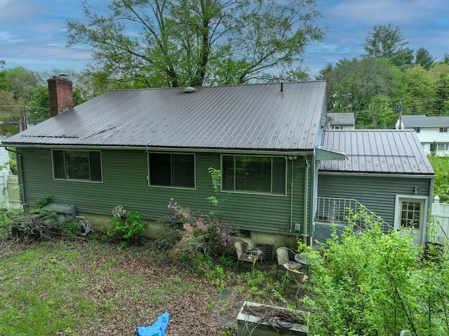 back of house with metal roof and a chimney