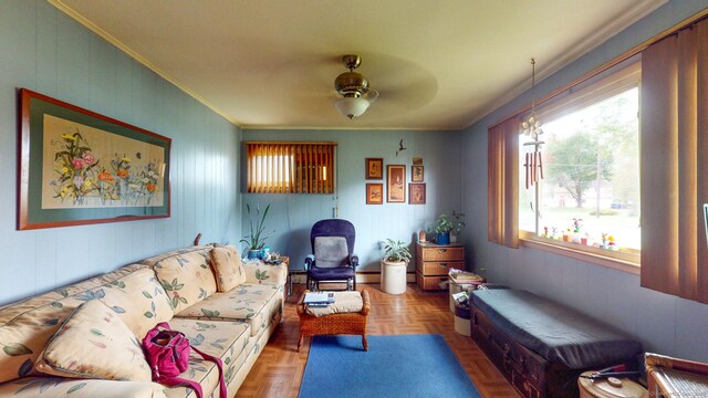 living area with crown molding, healthy amount of natural light, a ceiling fan, and wood walls