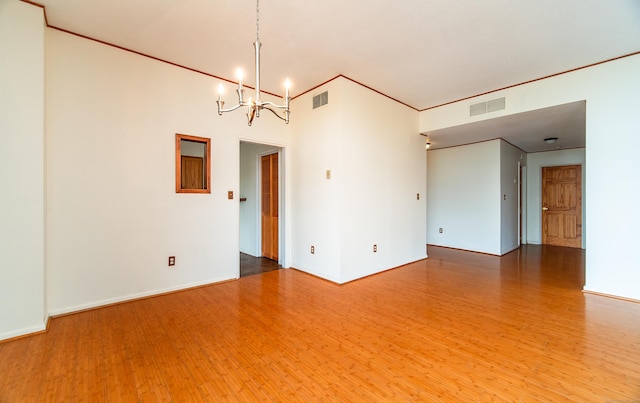 spare room featuring wood finished floors, a chandelier, crown molding, and baseboards