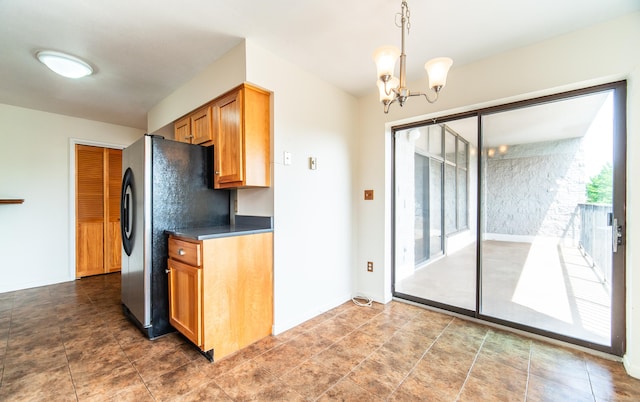 kitchen featuring dark countertops, freestanding refrigerator, a chandelier, brown cabinetry, and pendant lighting