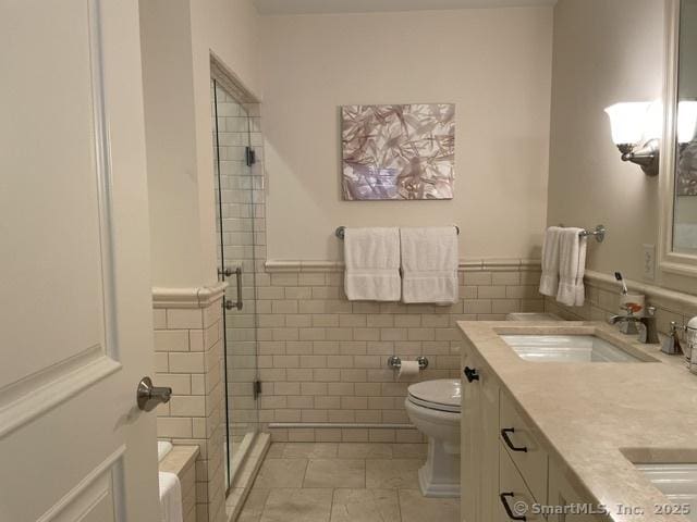 bathroom with tile walls, tile patterned floors, toilet, a stall shower, and a wainscoted wall