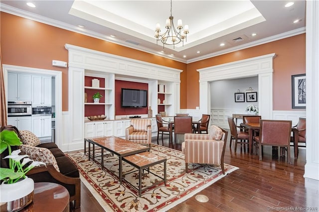 living room with crown molding, a chandelier, a wainscoted wall, a tray ceiling, and dark wood finished floors