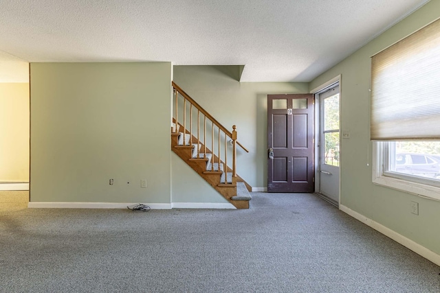 carpeted entrance foyer with a textured ceiling, stairway, and baseboards