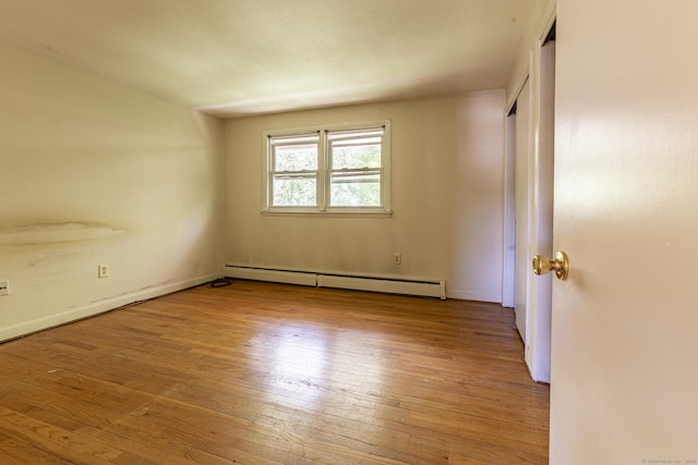 empty room featuring baseboard heating, wood finished floors, and baseboards