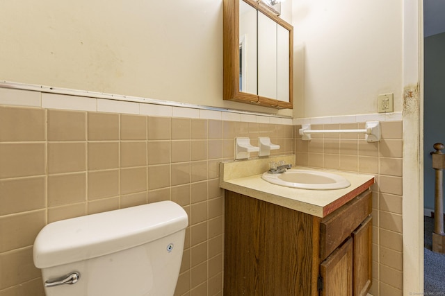 half bathroom with tile walls, vanity, toilet, and a wainscoted wall