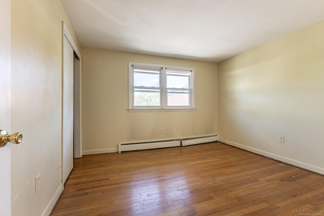 unfurnished bedroom featuring baseboard heating, wood-type flooring, baseboards, and a closet