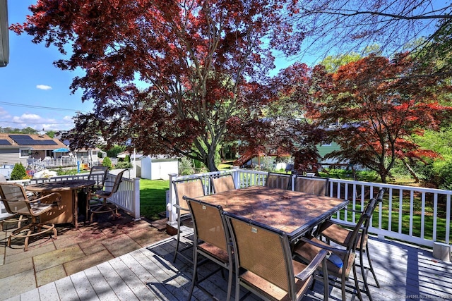wooden deck with outdoor dining space, a storage unit, and an outbuilding