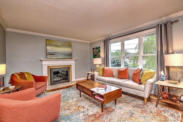 living area featuring wood finished floors, ornamental molding, a tiled fireplace, a textured ceiling, and baseboards