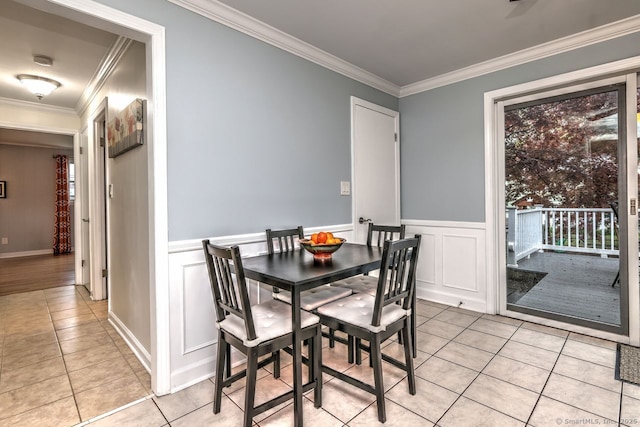 dining space with light tile patterned flooring, crown molding, a decorative wall, and a wainscoted wall