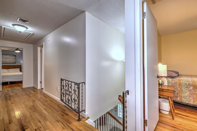 hall featuring an upstairs landing, wood finished floors, a textured ceiling, and baseboards
