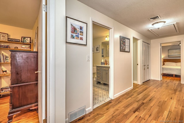 hall featuring light wood-style flooring, baseboards, and a textured ceiling