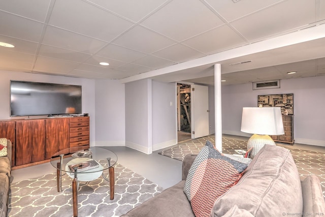 living room featuring a drop ceiling, baseboards, recessed lighting, and finished concrete floors