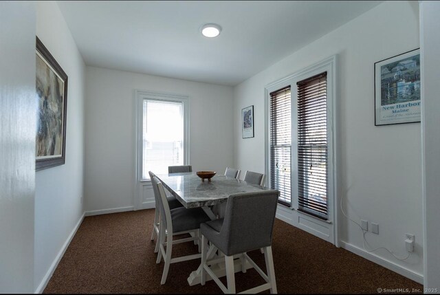 dining space featuring dark colored carpet, healthy amount of natural light, and baseboards
