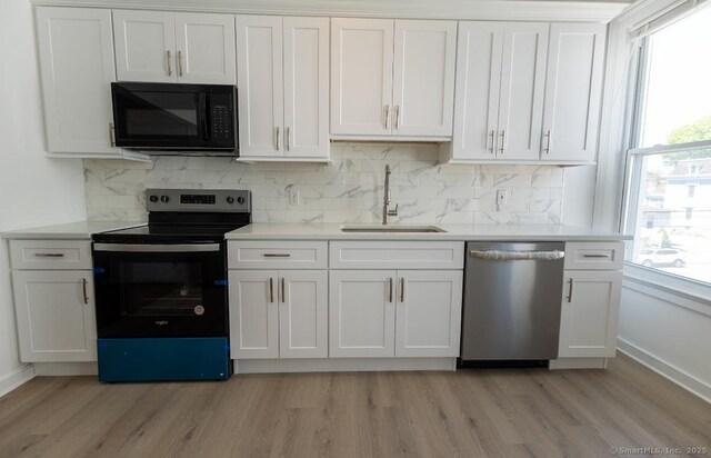 kitchen featuring black microwave, dishwasher, electric range, a sink, and light wood-style floors