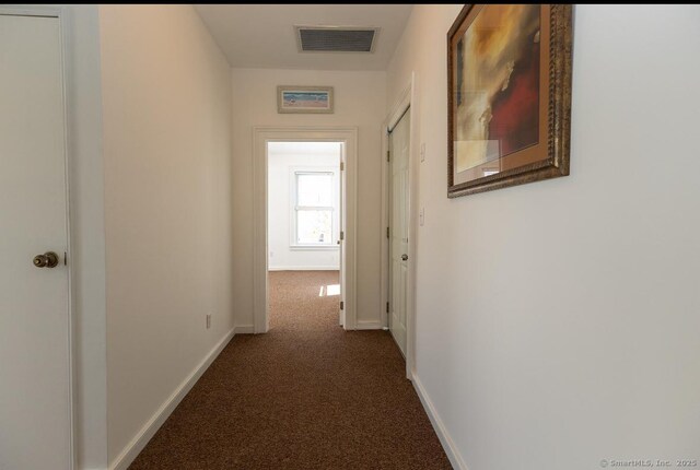 corridor featuring dark colored carpet and baseboards