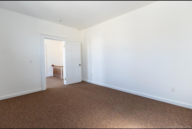 spare room featuring dark carpet and baseboards