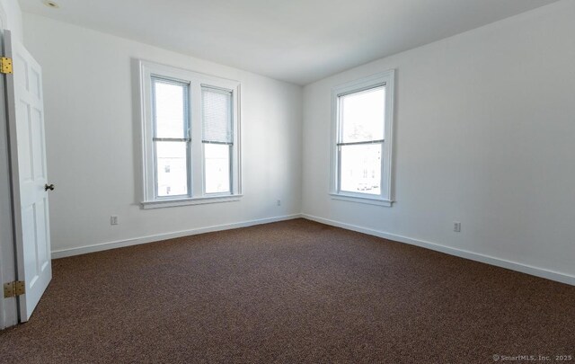 unfurnished room featuring plenty of natural light, dark carpet, and baseboards