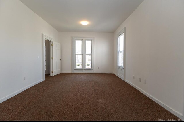 unfurnished room with baseboards and dark carpet