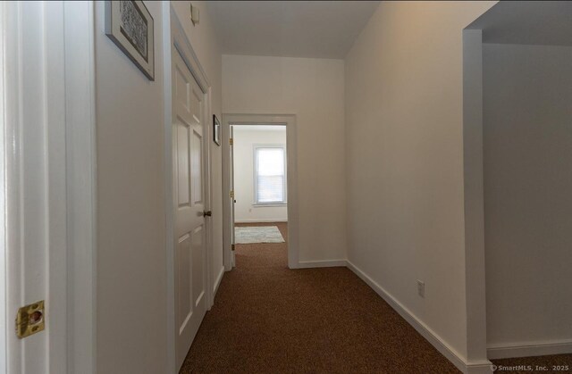 hallway featuring dark carpet and baseboards
