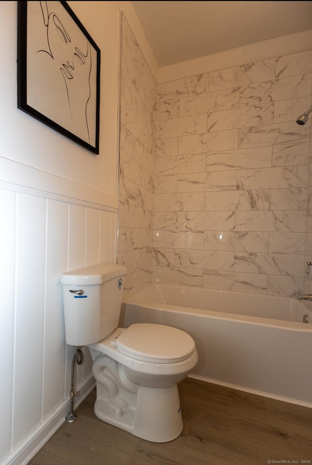 full bath with toilet, a decorative wall, wainscoting, shower / bath combination, and wood finished floors