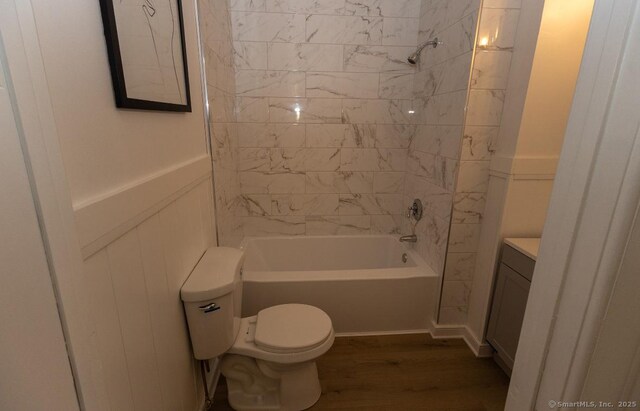 bathroom featuring wood finished floors, toilet, shower / bathtub combination, vanity, and a wainscoted wall