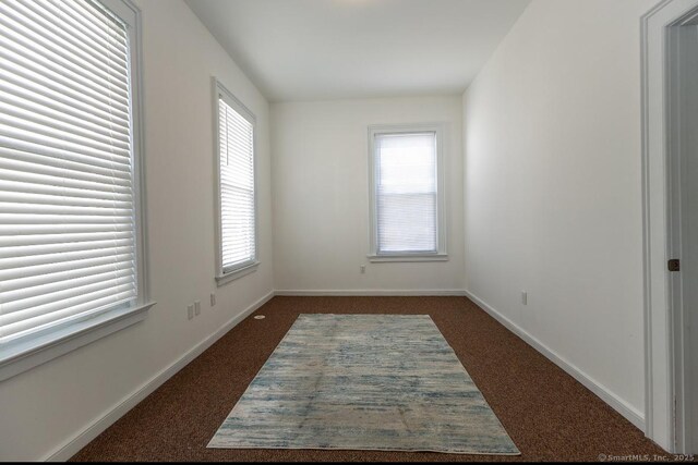 unfurnished room featuring dark carpet and baseboards