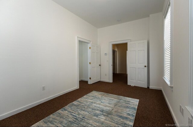 unfurnished bedroom featuring dark carpet and baseboards