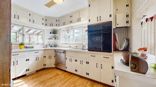 kitchen with oven, stainless steel dishwasher, a sink, light wood-style flooring, and light countertops
