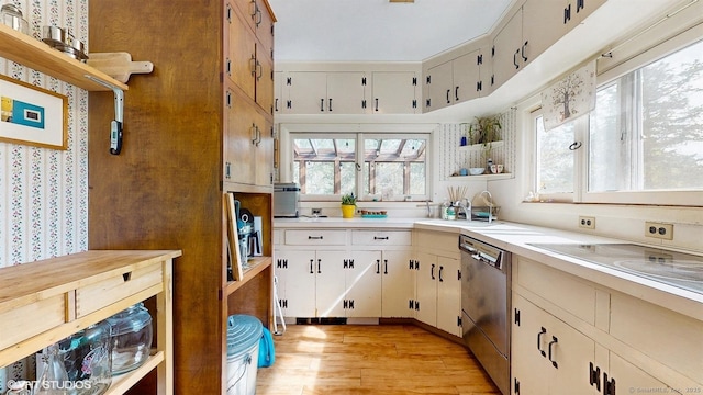 kitchen with stainless steel dishwasher, a sink, light countertops, and light wood finished floors