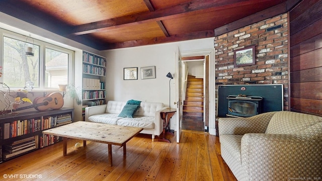 sitting room featuring hardwood / wood-style floors, beamed ceiling, a wood stove, and stairway