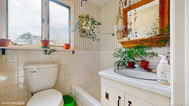 bathroom featuring wallpapered walls, toilet, tile walls, healthy amount of natural light, and vanity