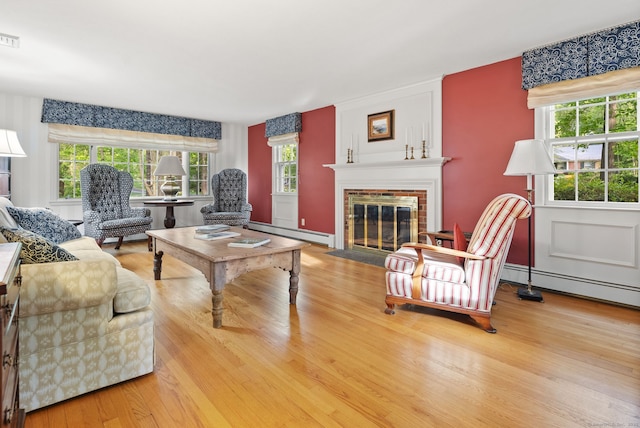 living area featuring a baseboard heating unit, a fireplace, and wood finished floors