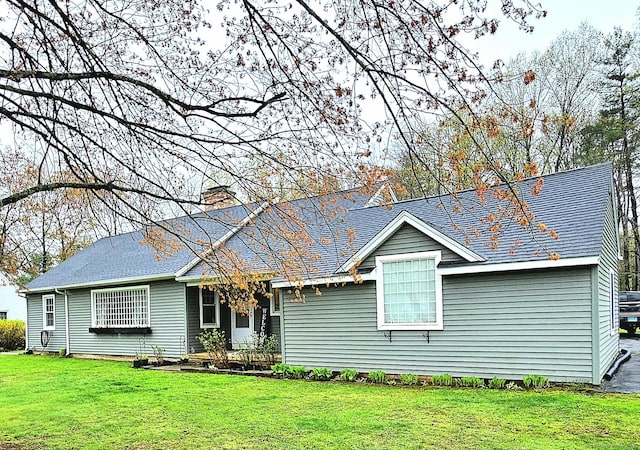ranch-style home featuring a front lawn, a chimney, and roof with shingles