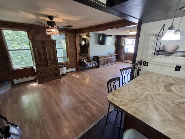 dining space featuring baseboard heating, wood finished floors, ceiling fan, and wooden walls