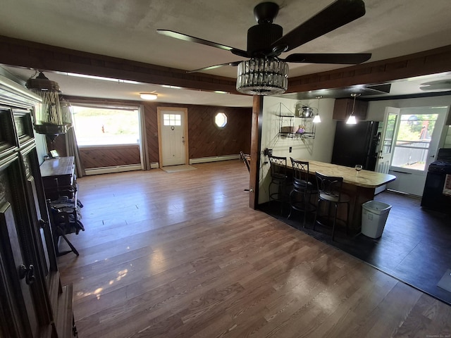 kitchen featuring freestanding refrigerator, wood finished floors, a ceiling fan, wood walls, and a baseboard heating unit
