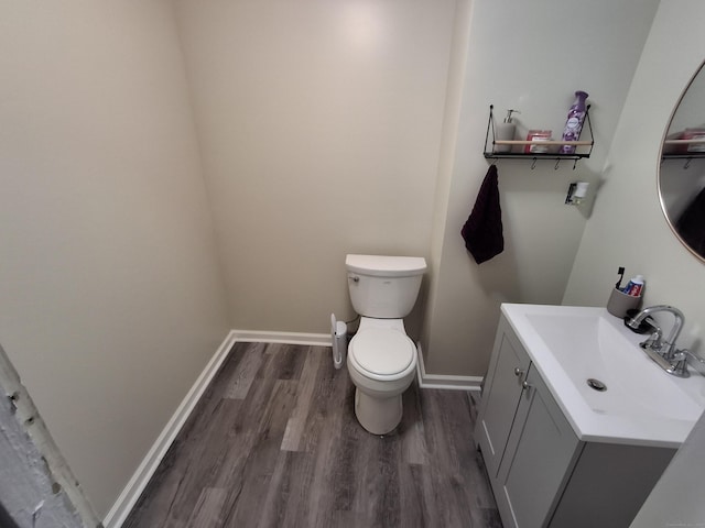 half bathroom featuring wood finished floors, vanity, toilet, and baseboards